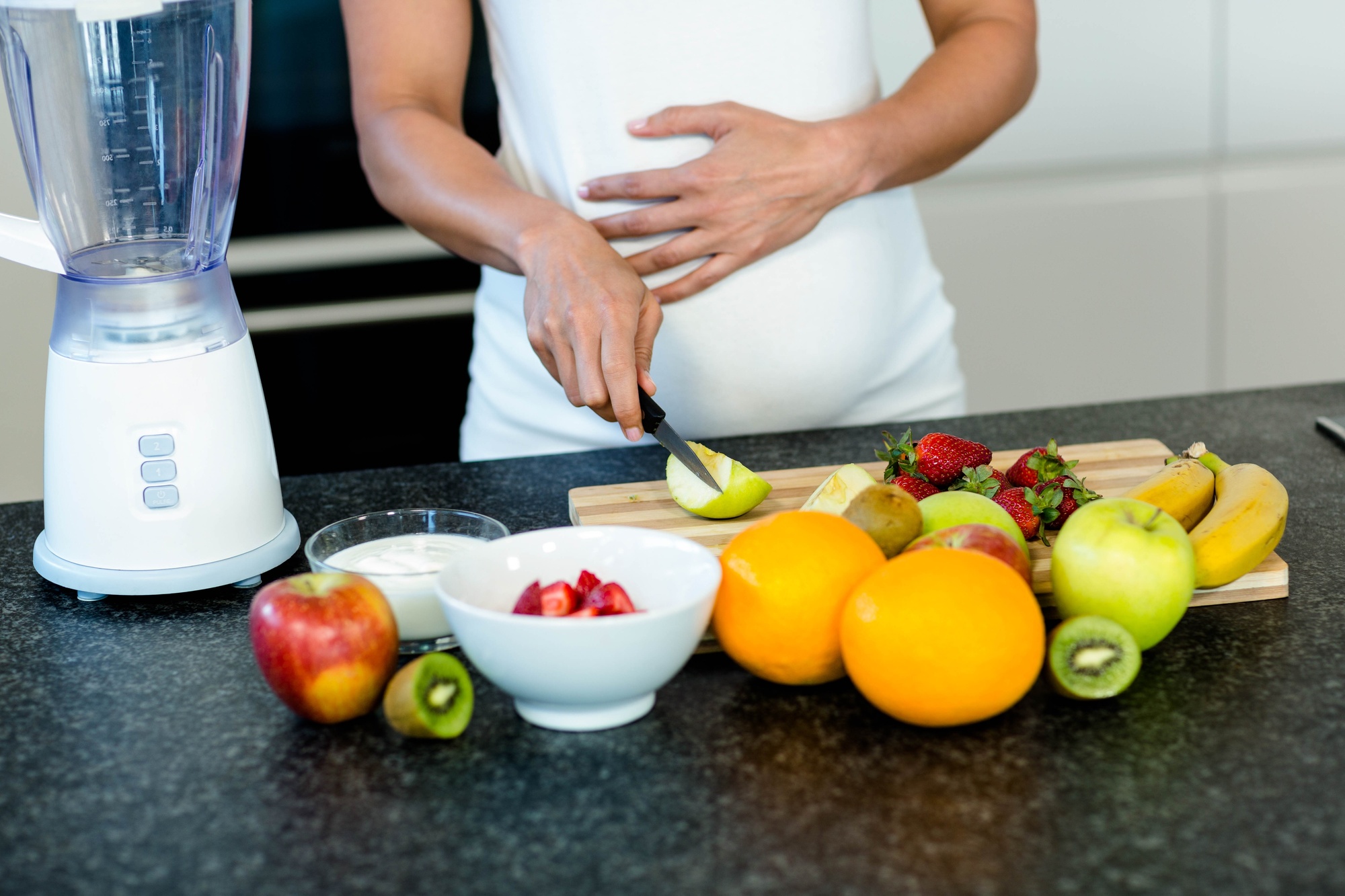 Pregnant woman touching her belly while cutting fruits